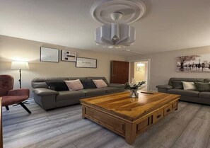 Una sala de estar con una mesa de centro de madera, dos sofás grises, un sillón rojo y un ventilador de techo.