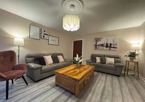 A living room with two grey sofas, a wooden coffee table, a pink armchair, and a floor lamp.