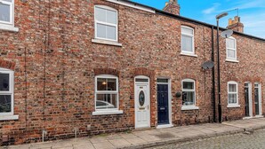 A two-story brick building with white-framed windows and doors, a satellite dish, and a cobblestone street. - 29 Carleton Street · Newly Refurbished 2-Bed Terraced Home in York - Pass the Keys (York)
