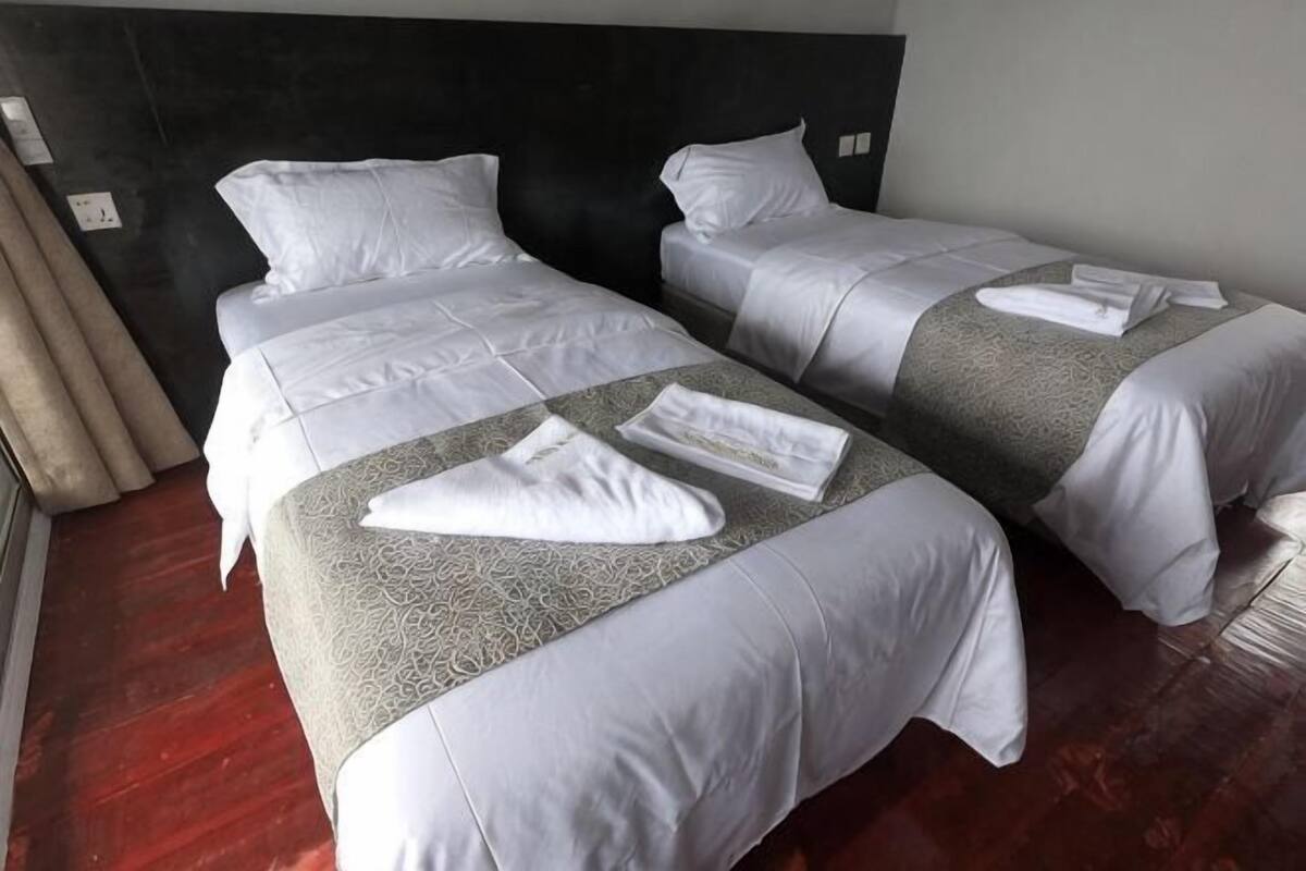 Habitació d'hotel amb dos llits, un capçal de llit fosc i un sòl de fusta.