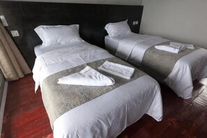 A hotel room with two beds, a dark headboard, and a wooden floor. - Mabul Backpackers (Tawau Division)
