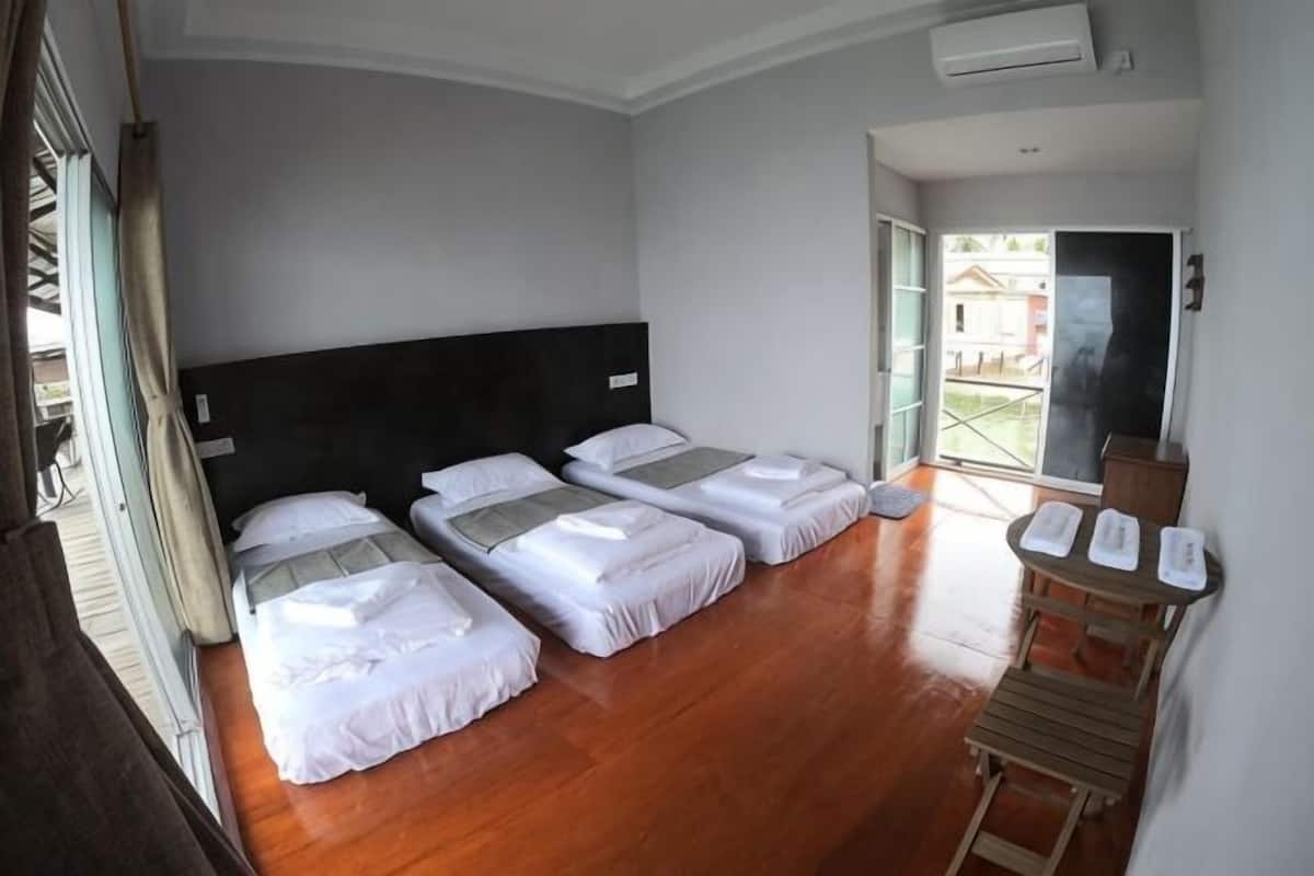 Habitació d'hotel amb tres llits, un sòl de fusta, una finestra gran i una porta corredissa que dona a un balcó.