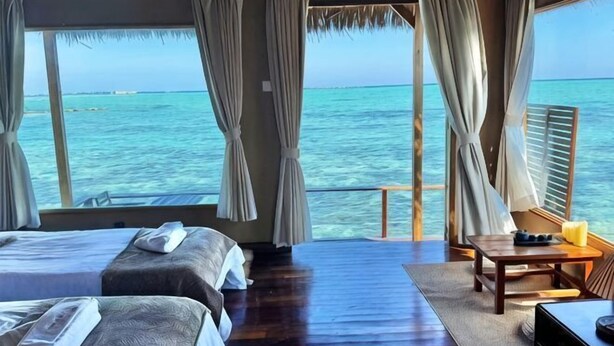 A room with two beds, a wooden floor, a table with a chair, and a view of the ocean. - Mabul Backpackers (Tawau Division)