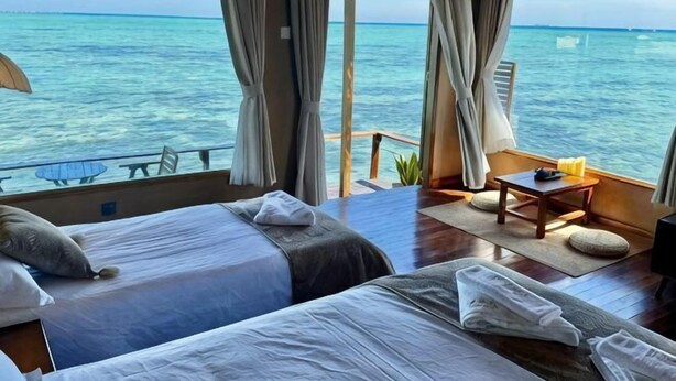 Een kamer met twee bedden, een klein tafeltje en uitzicht op zee.