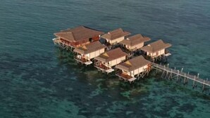 Luchtbeeld van waterwoningen met verschillende niveaus, verbonden door looppaden, en een boot op de achtergrond.