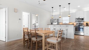 Una cocina moderna con armarios blancos, electrodomésticos de acero inoxidable y una mesa de comedor de madera con sillas.