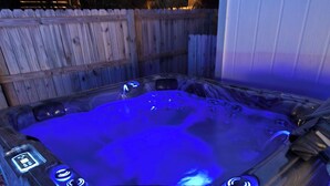 Ein Whirlpool mit digitaler Bedieneinheit, umgeben von einem Holzzaun und einem Gebäude im Hintergrund.