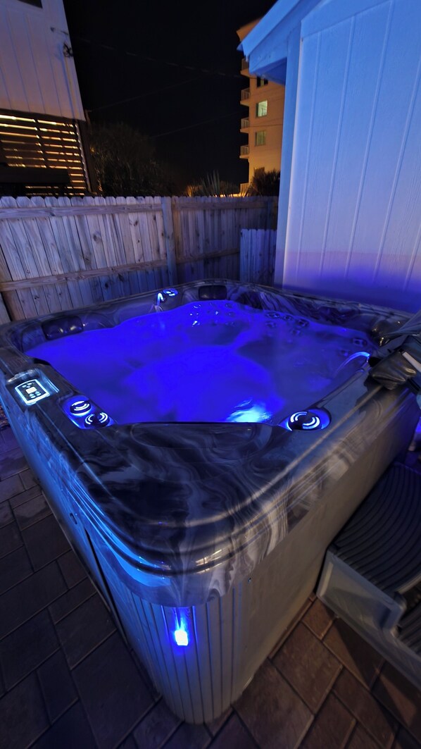 Un jacuzzi con panel de control digital, rodeado por un cerco de madera y un edificio al fondo.