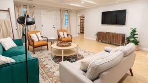 En rummelig stue med sofa, to lænestole, sofabord og et tv ophængt på væggen.