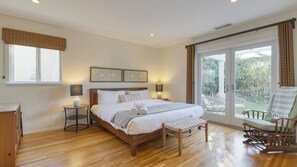 A bedroom with a wooden bed, two bedside tables, a bench, a rocking chair, and a view of the outdoors. - Goleta Getaway by Avantstay Private Backyard, 1.5mi to the Beach! (Goleta)