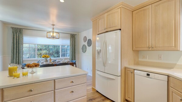 A kitchen with wooden cabinets, a white refrigerator, a Bosch dishwasher, and a dining area with a table set for breakfast. - Goleta Getaway by Avantstay Private Backyard, 1.5mi to the Beach! (Goleta)