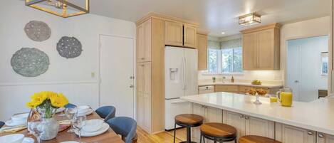 A modern kitchen with wooden cabinets, a white refrigerator, and a large island with stools.