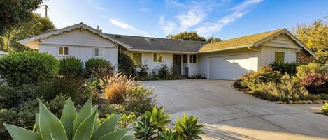 A two-story house with a front driveway, a garage, and a well-maintained garden with various plants.