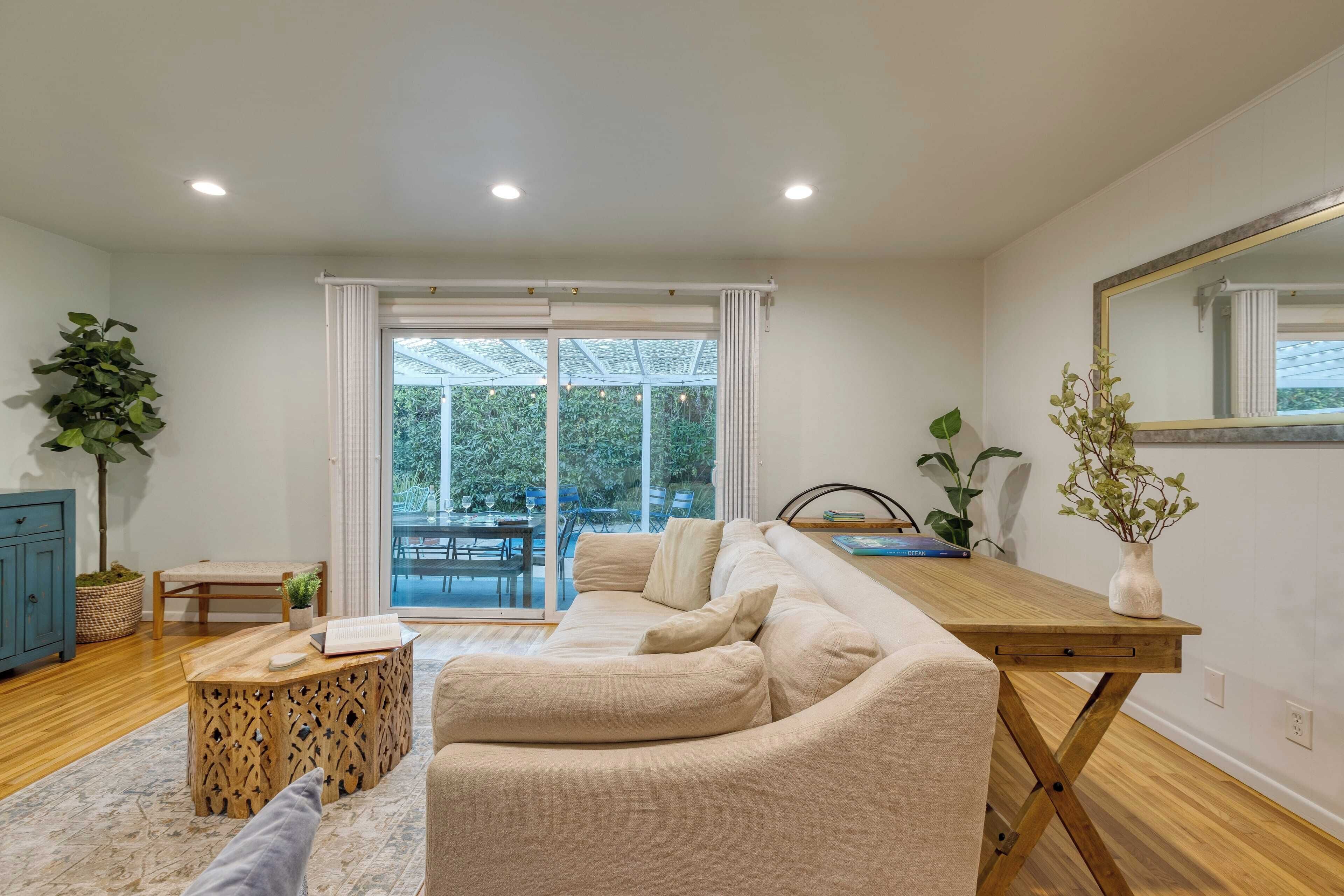 A modern living room with a beige sofa, wooden coffee table, and a large window with curtains.