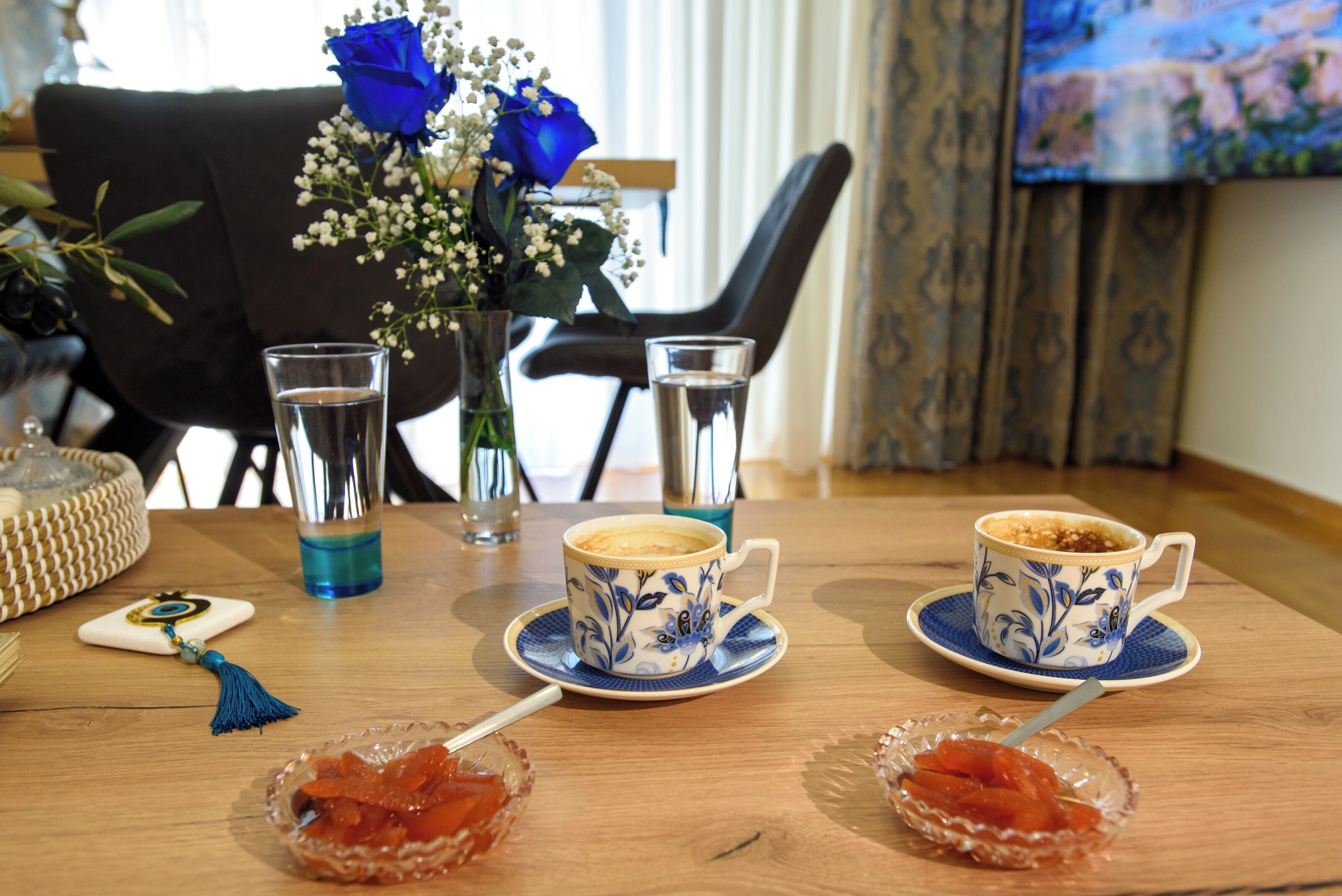 A wooden table with two cups of coffee, a glass of water, and two bowls of jam.