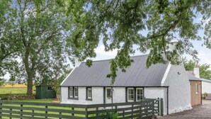 A white building with a grey roof, surrounded by a wooden fence and trees.