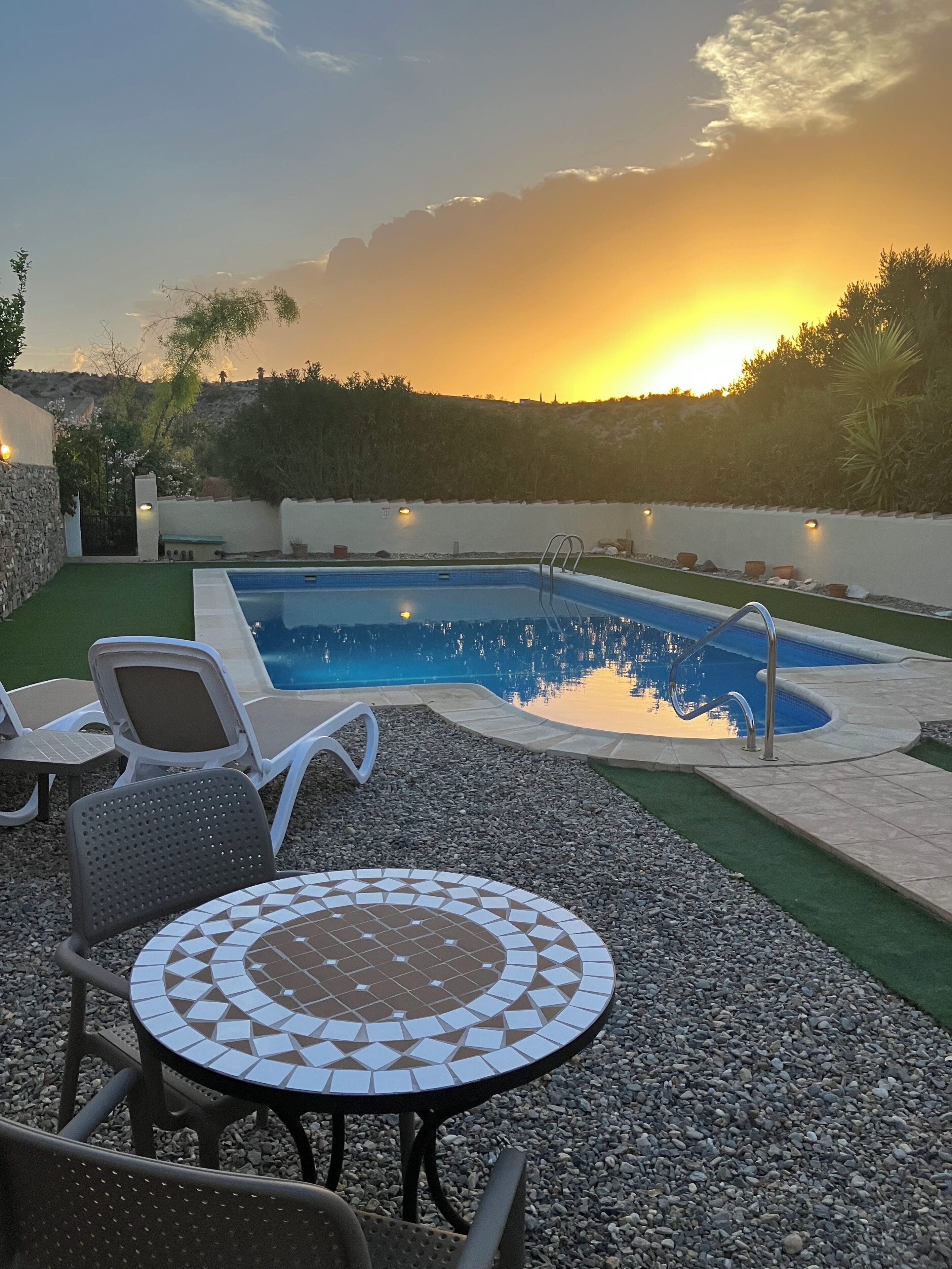 Una piscina amb una terrassa enrajolada, envoltada d'un pati amb cadires i una taula.