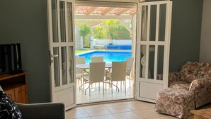 Un espacio de sala abierto con vistas a una piscina, un sofá, un televisor y una alfombra estampada.