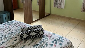 Un dormitorio con cama, armario, ventana con cortinas y suelo de baldosas.