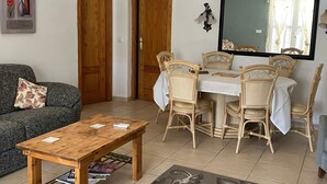 Una sala de estar con una mesa de centro de madera, un sofá, una mesa de comedor con sillas, un espejo grande y un ventilador de techo.