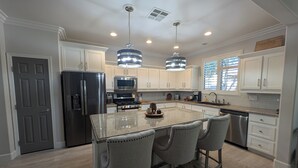 Una cocina moderna con armarios blancos, un refrigerador de acero inoxidable, un microondas y una isla de granito con taburetes de bar.
