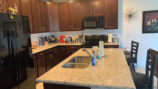 A kitchen with dark wooden cabinets, a black refrigerator, a microwave, and a granite countertop.