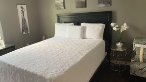 A neatly made bed with a white bedspread, a dark headboard, and a small round table with a vase of white flowers.