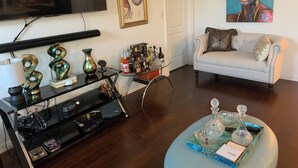 A living room with a sofa, a glass coffee table, a TV, and a painting on the wall.