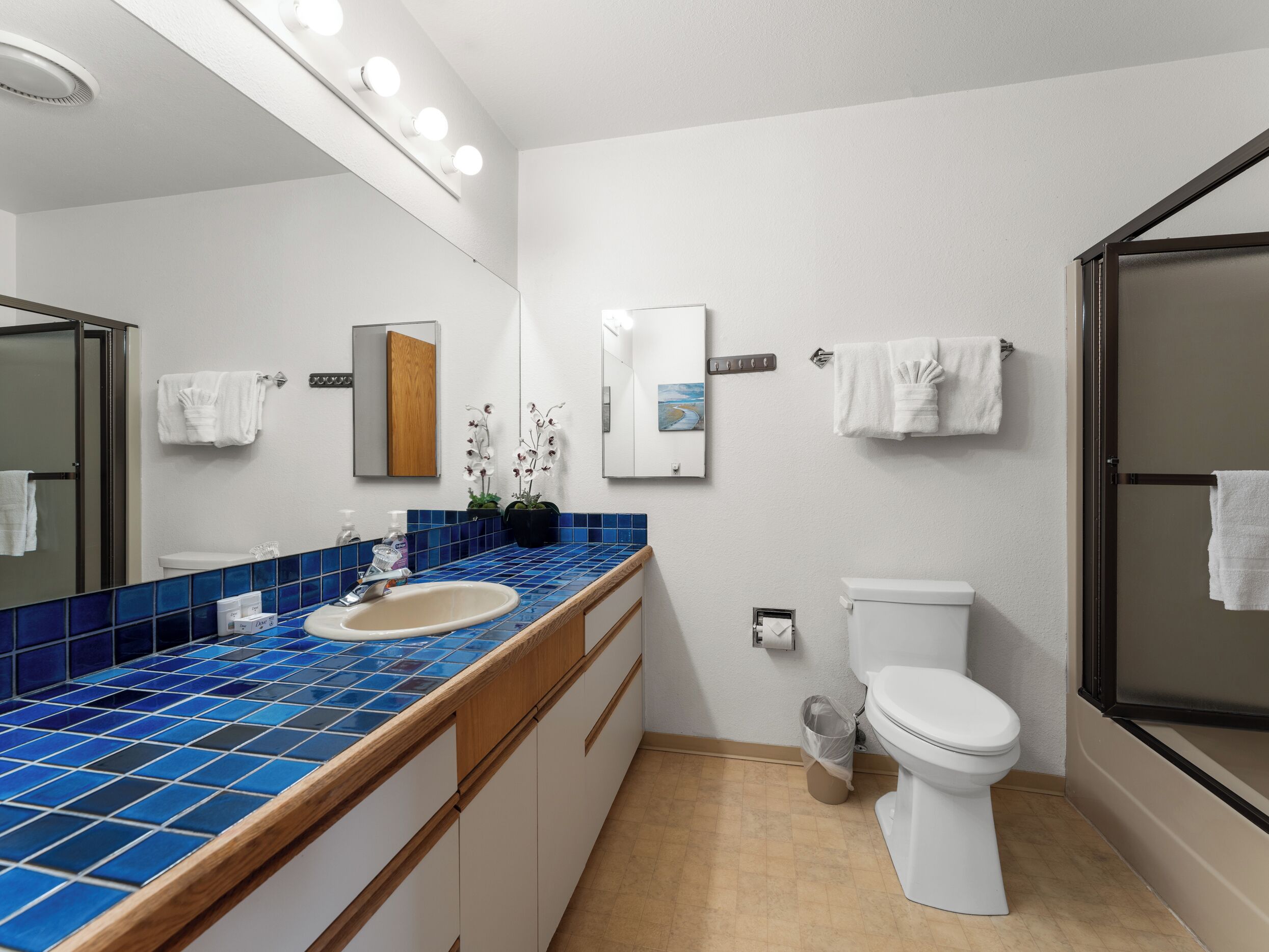 A bathroom with a blue-tiled sink, a white toilet, and a glass-enclosed shower.