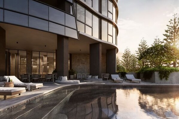 Un área de piscina moderna al aire libre con sillones de descanso y una estructura de edificio curvada.