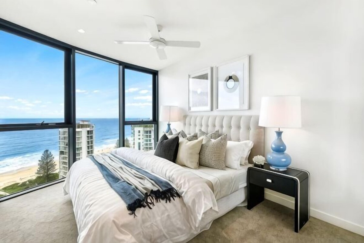 A bedroom with a large bed, a nightstand, a ceiling fan, and a view of the ocean.