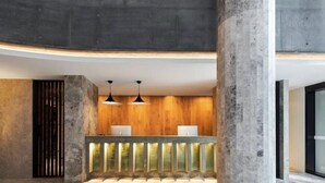 A reception area with a wooden panel wall, a reception desk with two white lamps, and a concrete pillar. - Vue Broadbeach - Official (Broadbeach)
