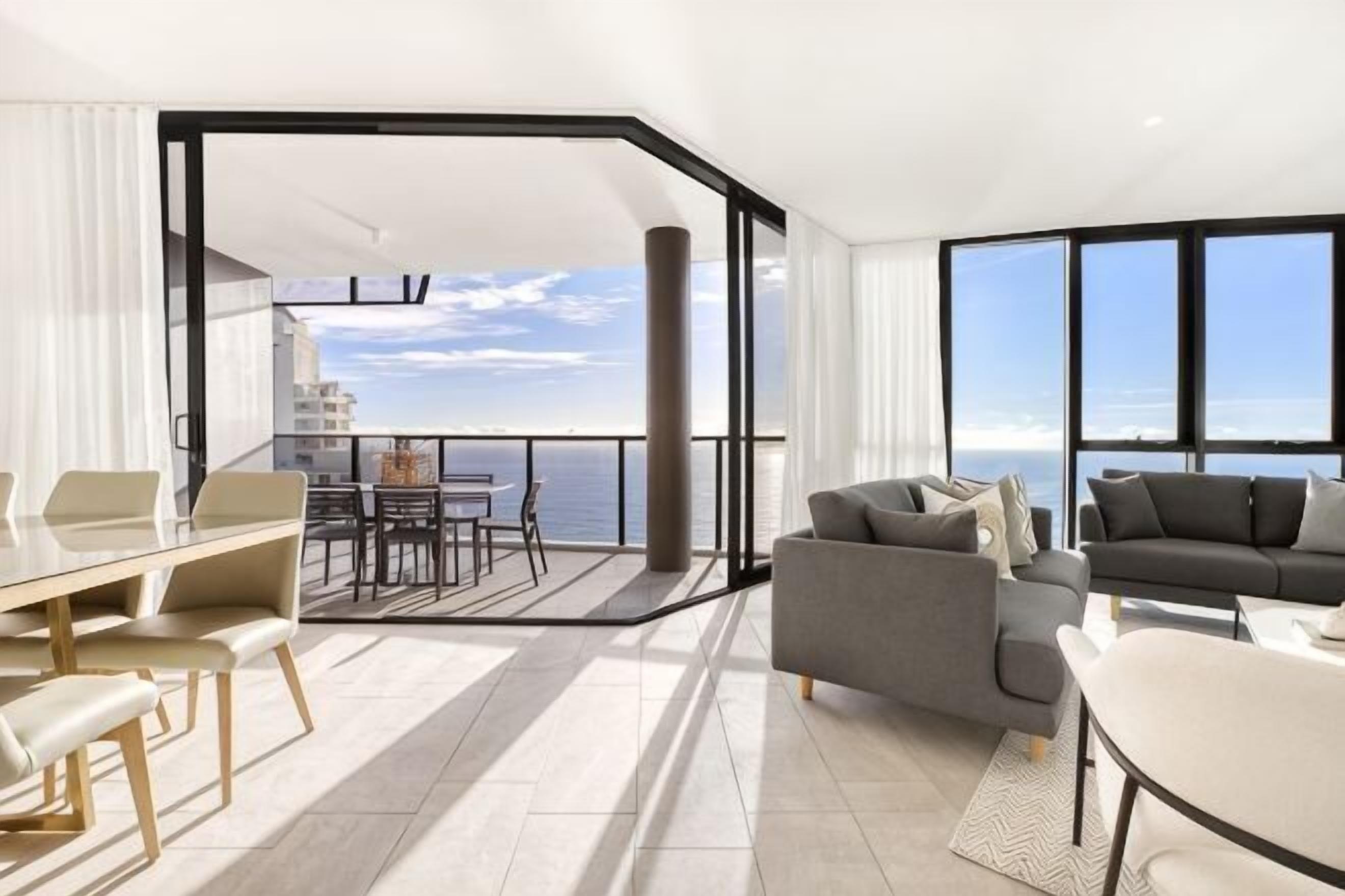 A modern interior with a balcony, a dining area, and a seating area with a view of the sea.