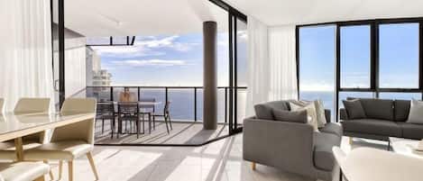 A modern interior with a balcony, a dining area, and a seating area with a view of the sea.