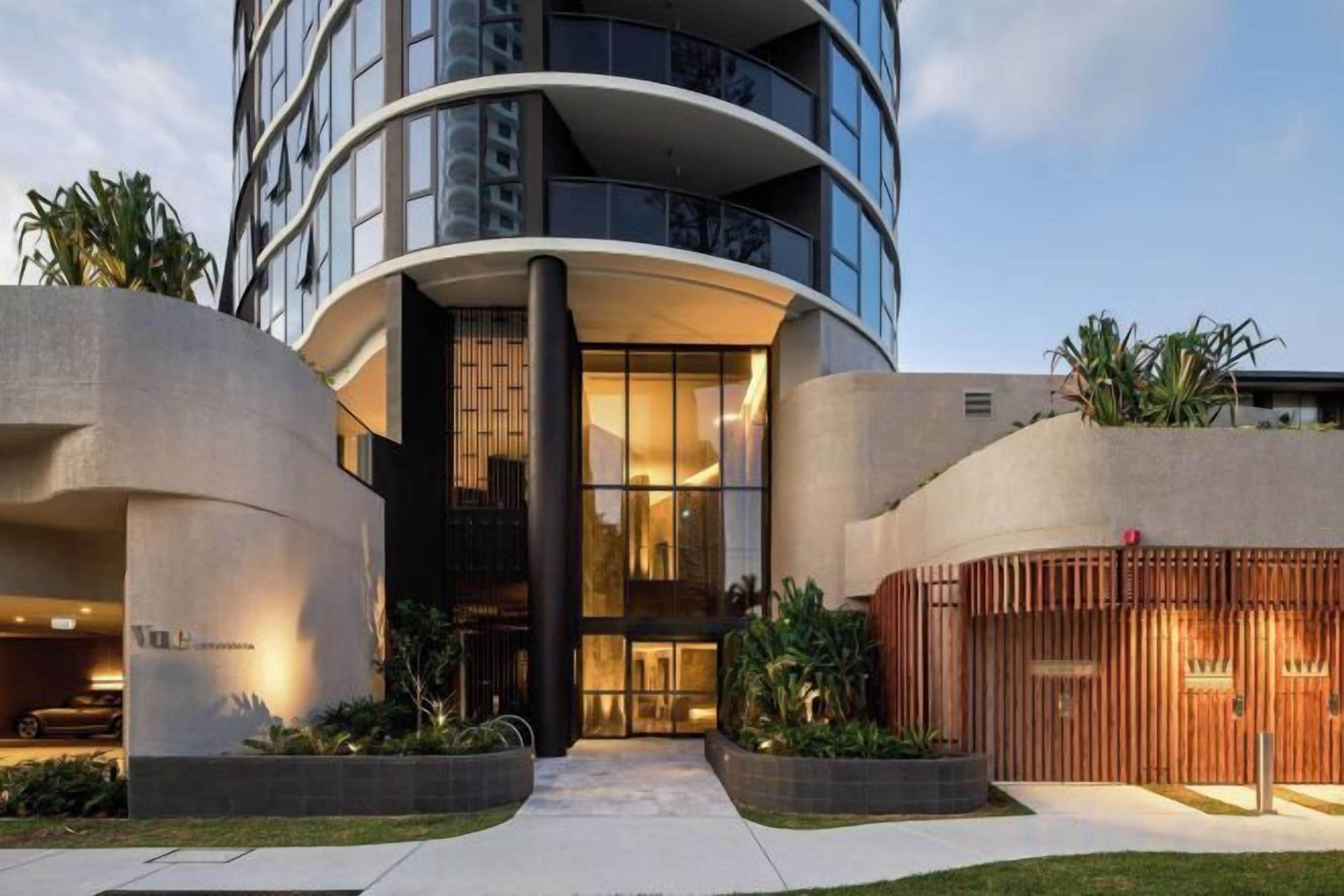 Un hôtel moderne à la façade incurvée, doté de grandes fenêtres et d’une entrée bien éclairée.
