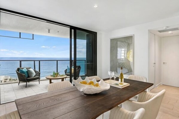 Un espace repas moderne avec une table en bois, des chaises blanches et une vue sur la mer.