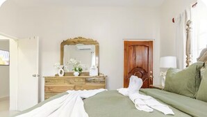 Un lit bien fait, avec du linge de lit blanc, une commode en bois avec un miroir et un canapé vert.