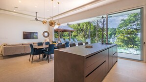 A modern kitchen with a large island, dining area, and a view of a lush garden.