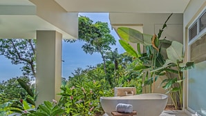 Ein modernes Badezimmer im Freien mit einer großen Badewanne, einem hölzernen Hocker und üppigem Grün.