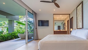 Ein modernes Schlafzimmer mit einem großen Bett, einem Deckenventilator, einem Fernseher und einer Glastür, die auf einen Balkon mit Grünpflanzen führt.