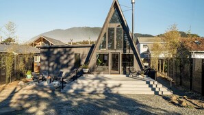 A modern house with a triangular roof, a staircase leading to the entrance, and a patio area with outdoor furniture.