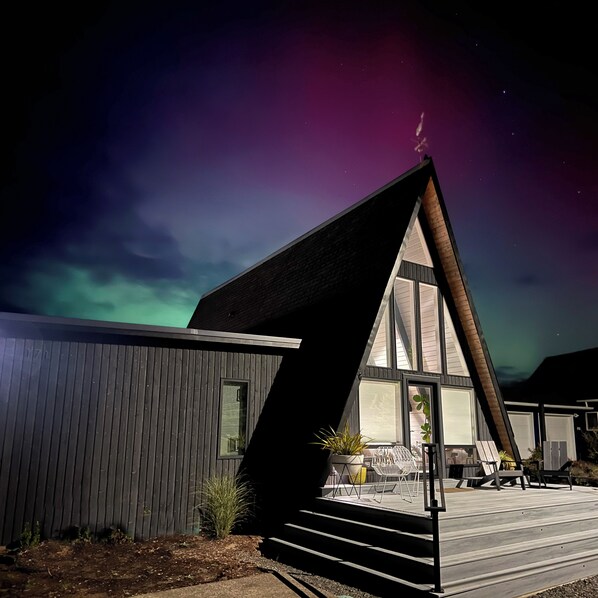 A modern house with a sloped roof and large windows, featuring a deck with outdoor seating.