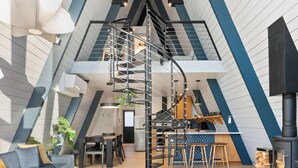 A modern loft with a high ceiling, a central staircase, a kitchen area, and a seating area with a sofa and coffee table.