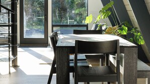 A modern dining area with a large table, chairs, and hanging plants.