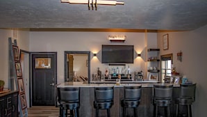 A bar area with a sign reading "COCKTAILS," a flat-screen TV mounted above the bar, and a wooden bar counter with stools. - Luxury Meets Historic @ The Luxe Loft - AMAZING LOCATION! (Algoma)