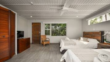 A modern bedroom with two beds, a wooden wardrobe, a television, and a large window with a view of greenery.