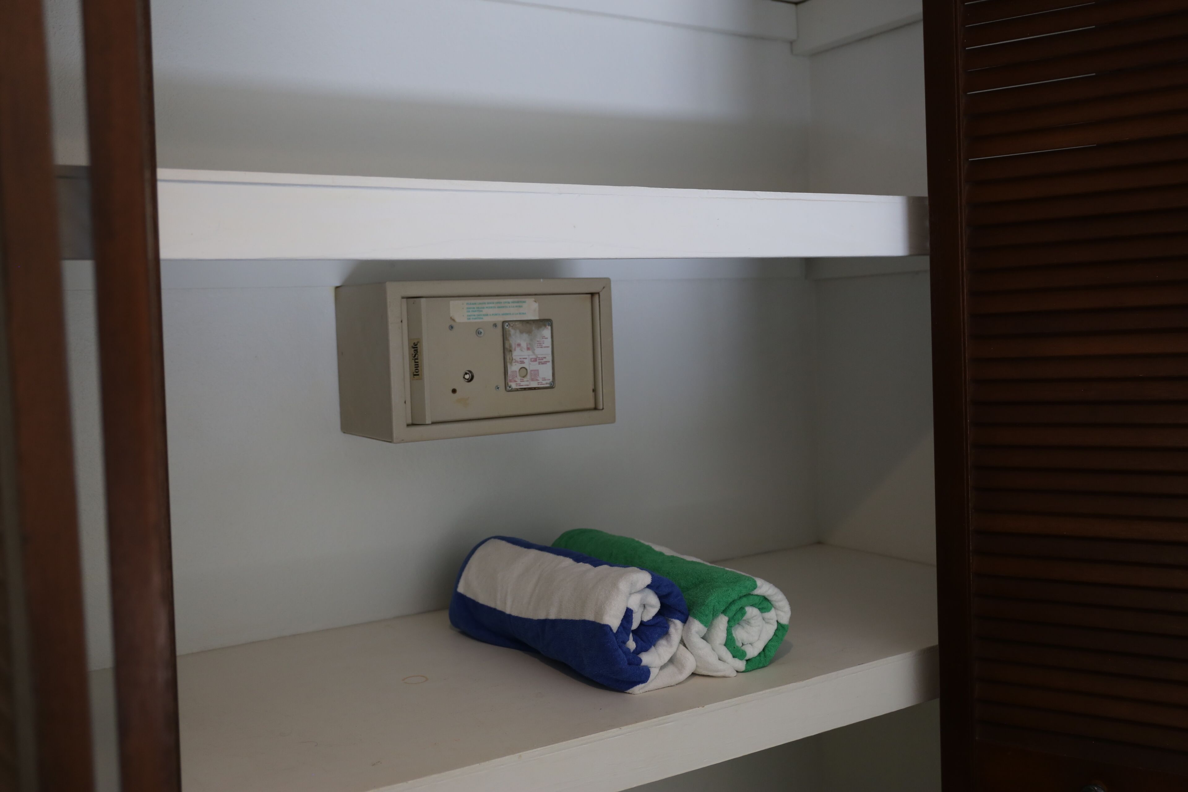 A room with a white shelf, a thermostat, and a rolled-up blanket.
