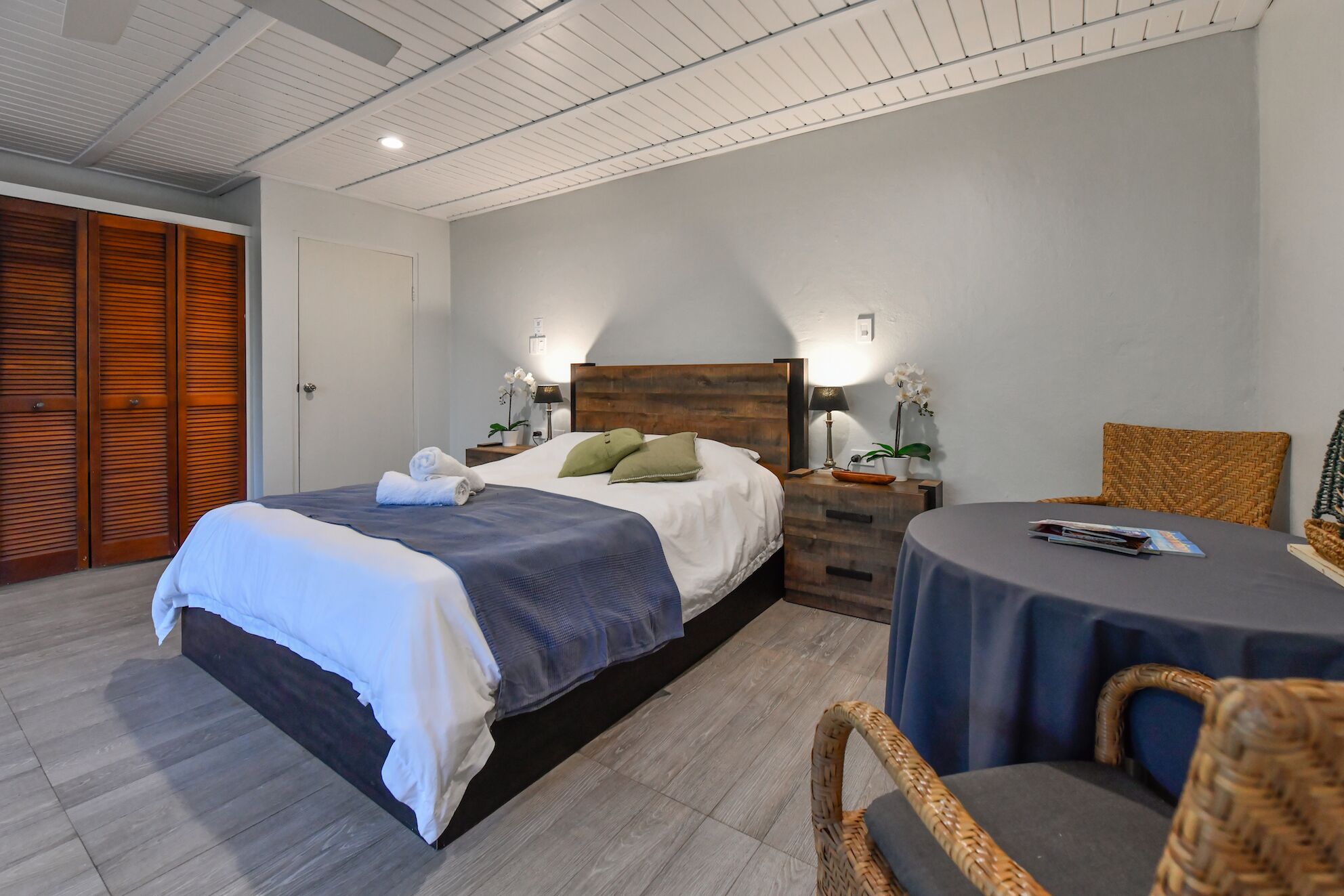 A hotel room with a large bed, a bedside table with a lamp, a chair, and a small table with a book.