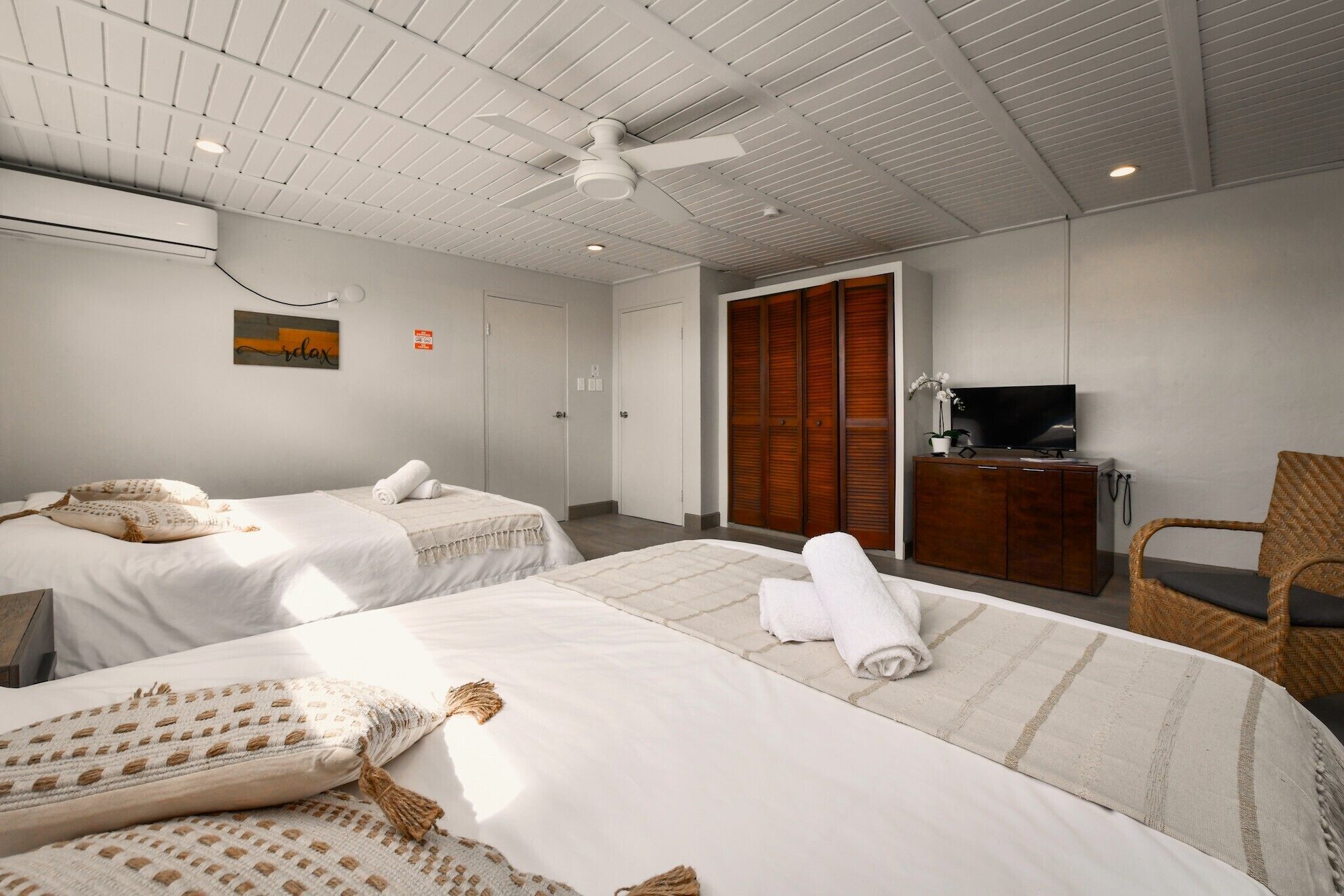 A hotel room with two beds, a television, a wardrobe, and a ceiling fan.