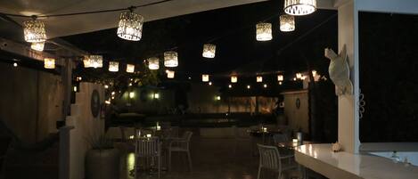 An outdoor seating area with tables and chairs, overhead lighting, and a statue on the right.